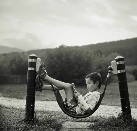 A boy reading a book while lounging in a tire swing in the countryside